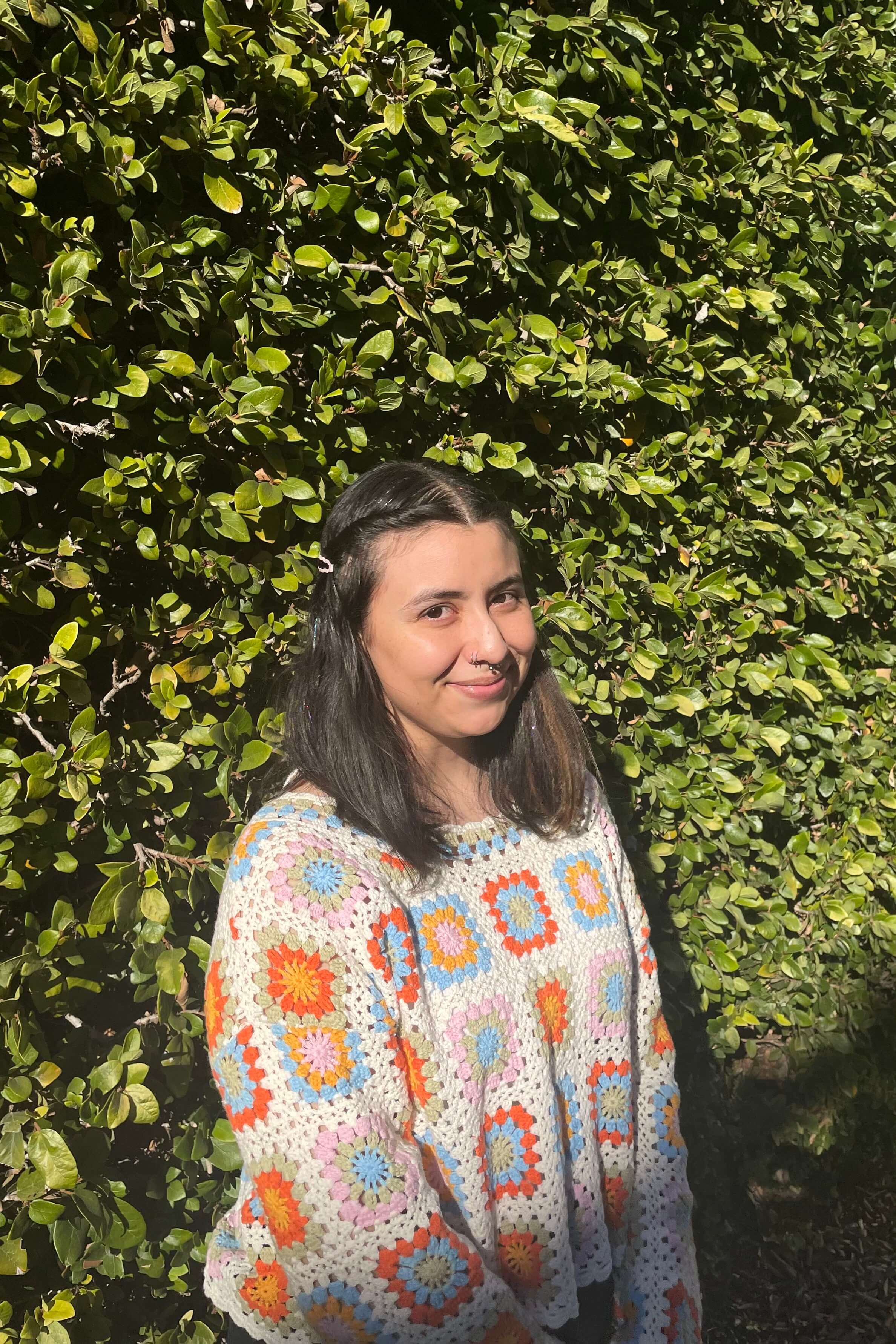 Natalia, Basic Needs Center Rapid Rehousing Coordinator, smiling at the camera in front of a leafy background.