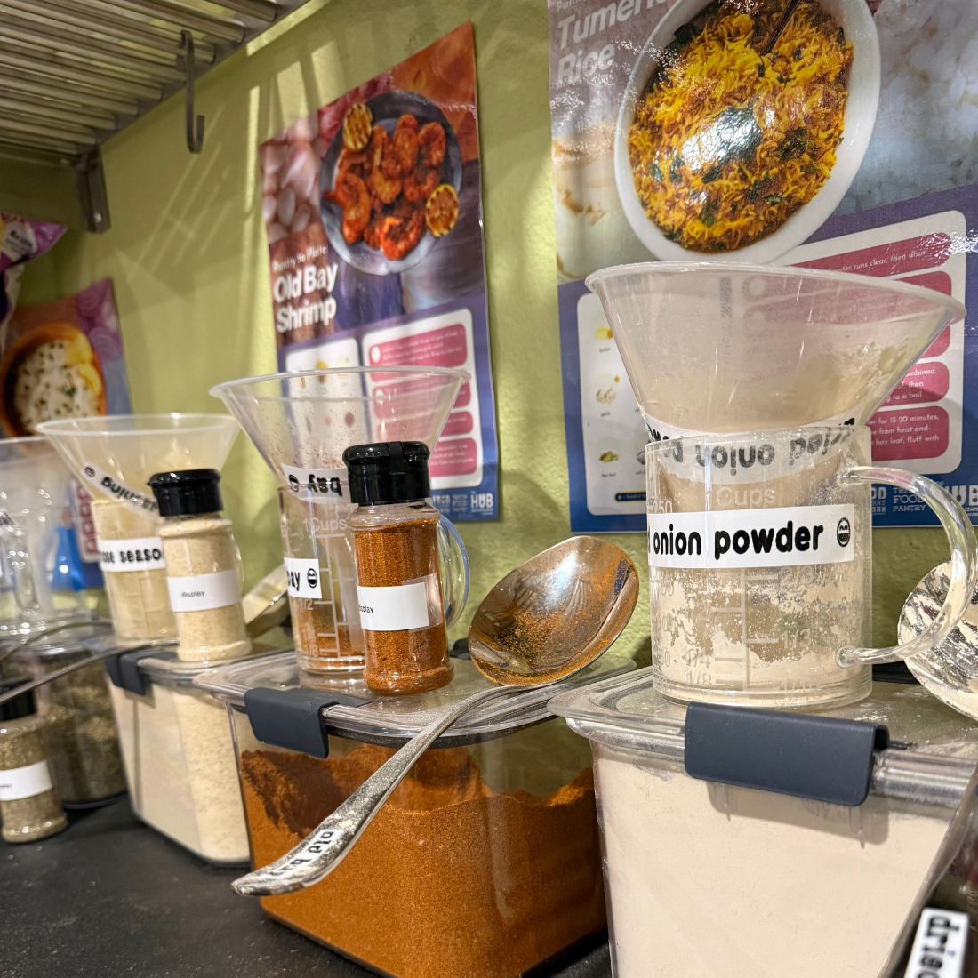 Shelf with spice jars and spoons, including onion powder and paprika.