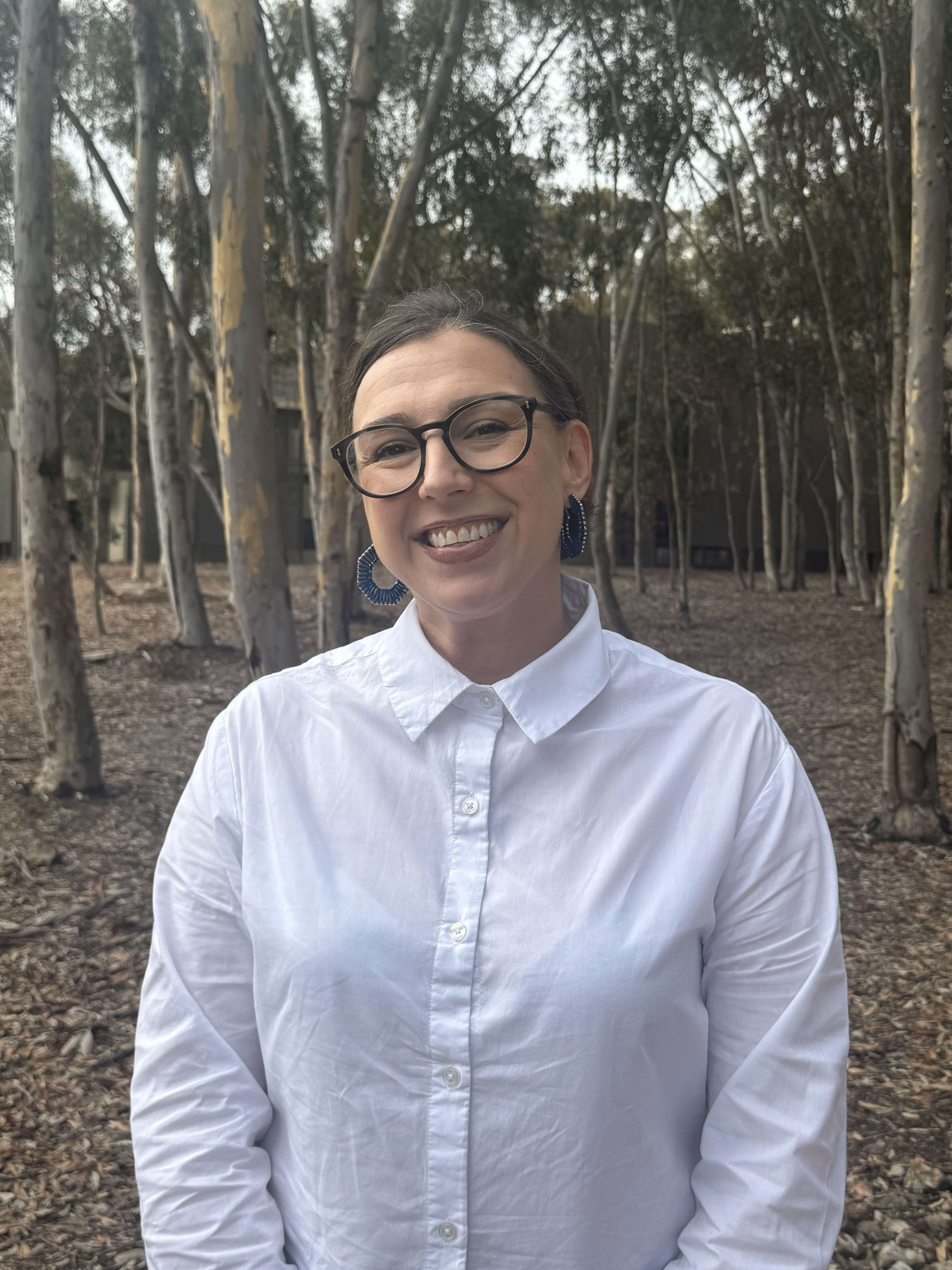 Alicia, Director of Basic Needs, smiling at the camera in front of a leafy background