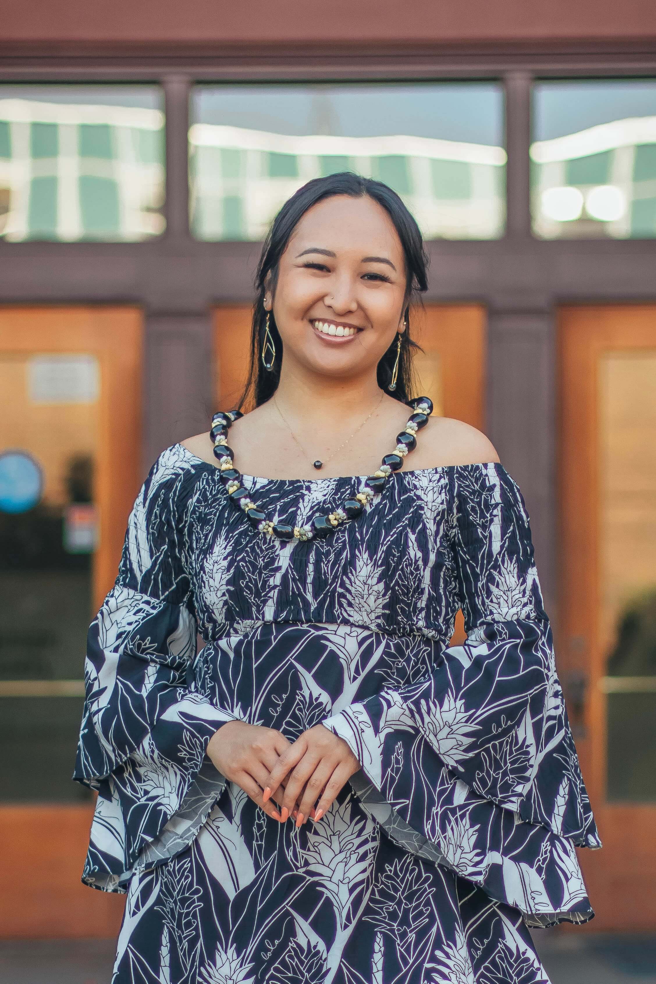 Haley Okamoto, Assistant Director of Food Security Program, smiling at the camera standing in front of an orange building