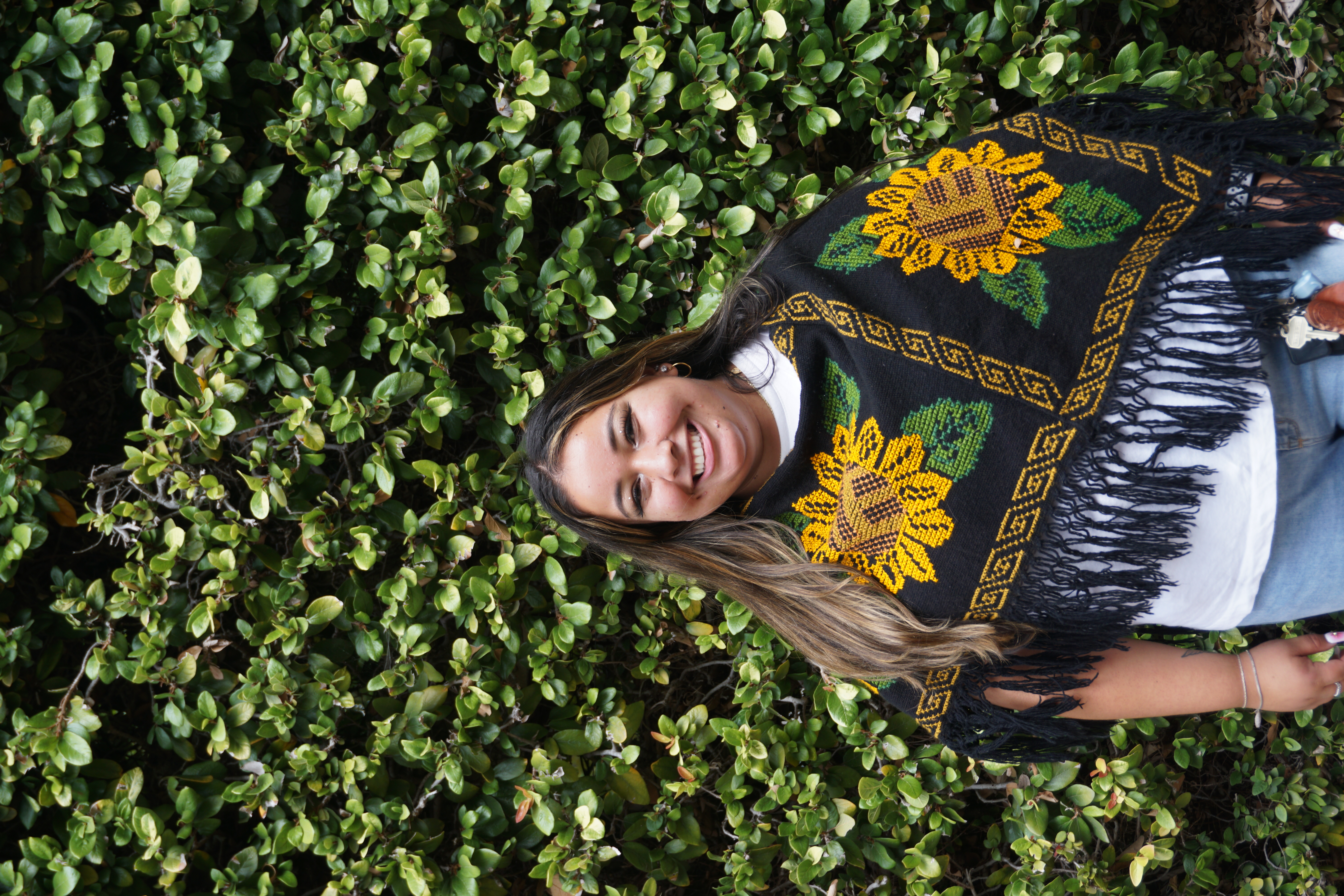 Maria Carmen, Basic Needs Program Coordinator, smiling at the camera in front of a leafy background